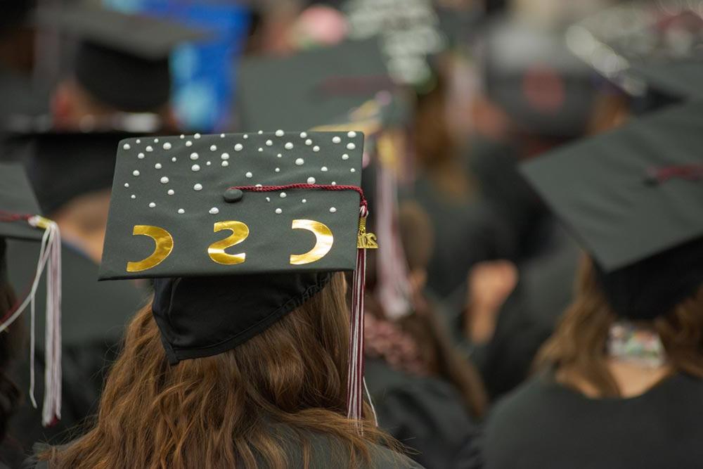 Student at graduation with a cap decorated to read CSC